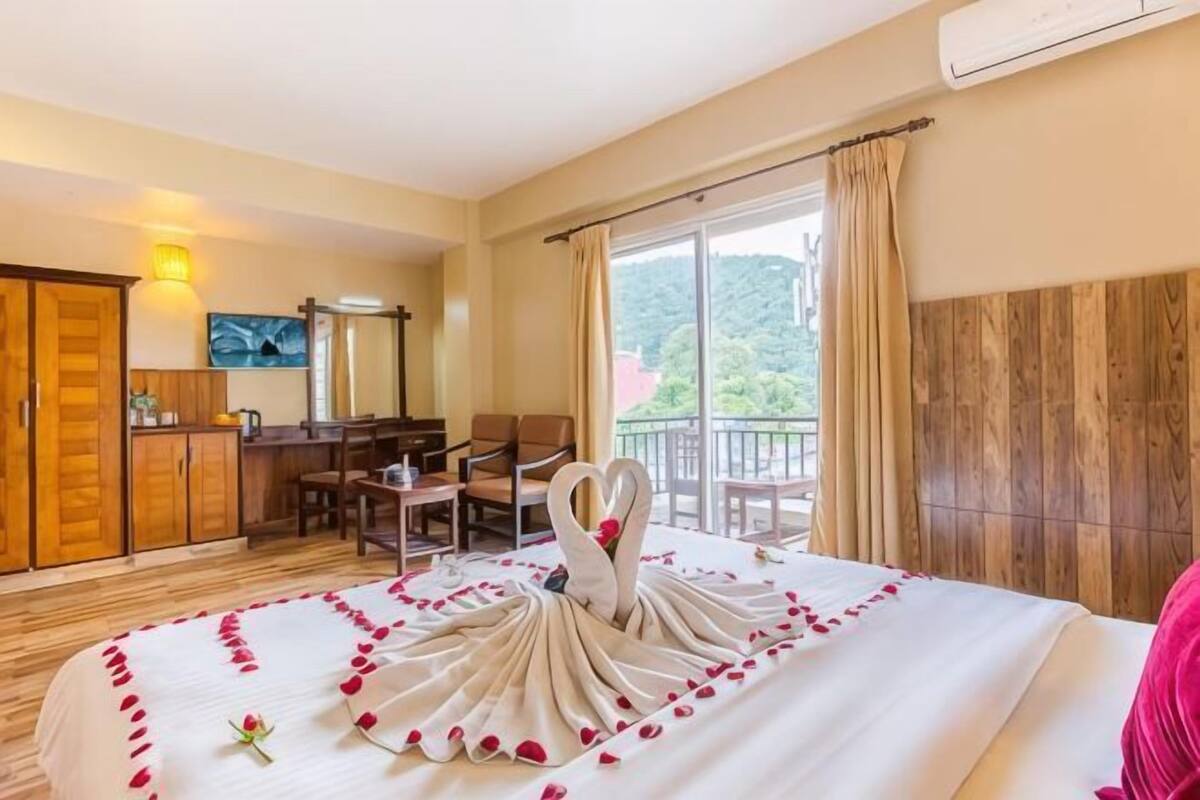A hotel room with a bed, a desk, a chair, a wardrobe, and a balcony with a view.