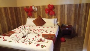 Une chambre d’hôtel avec une tête de lit en bois, un lit bien fait agrémenté d’un coussin en forme de cœur, et une table de chevet avec un téléphone.