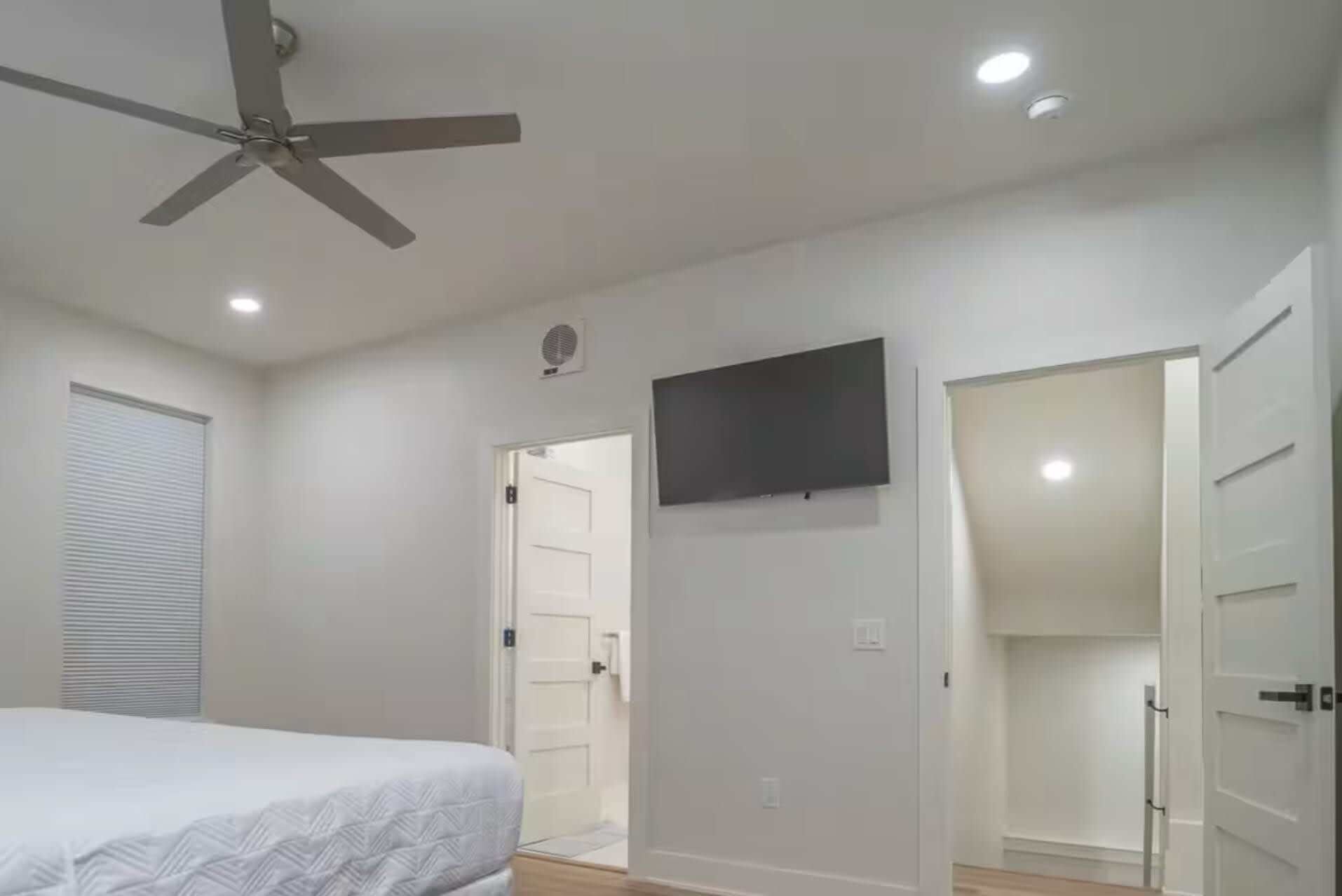 A bedroom with a bed, a ceiling fan, a TV mounted on the wall, and a closet with sliding doors.