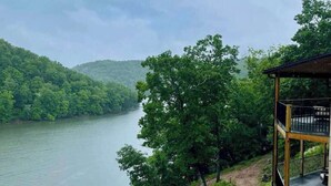 Une vue sur le fleuve, avec une terrasse en bois donnant sur un cours d’eau paisible, le tout entouré d’une végétation luxuriante et de collines.