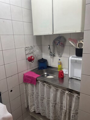 Una cocina con un lavamanos, una cafetera, una botella de detergente y un cubo de basura azul.