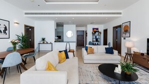Una sala de estar moderna con un sofá, una mesa de centro y un comedor. Se observa una cocina al fondo.