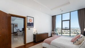 Un dormitorio con un ventanal grande, una cama, una mesita de noche, un aparador y un cuadro enmarcado en la pared.