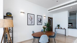Un comedor moderno con una mesa redonda de madera, seis sillas y un jarrón con flores. Hay dos cuadros en la pared, una lámpara y una planta en maceta.