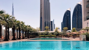 Una piscina con lettini e palme, circondata da edifici moderni.