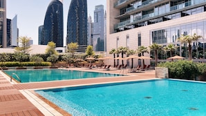 Una piscina con lettini e ombrelloni, circondata dal verde e da edifici moderni.