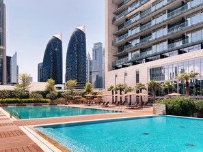 Ein Pool mit Liegestühlen und Sonnenschirmen, umgeben von Grünflächen und modernen Gebäuden.