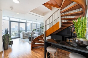 Ein modernes Interieur mit einer Wendeltreppe, einem Wohnbereich mit einer Couch und einem großen Fenster mit Blick auf die Stadt.