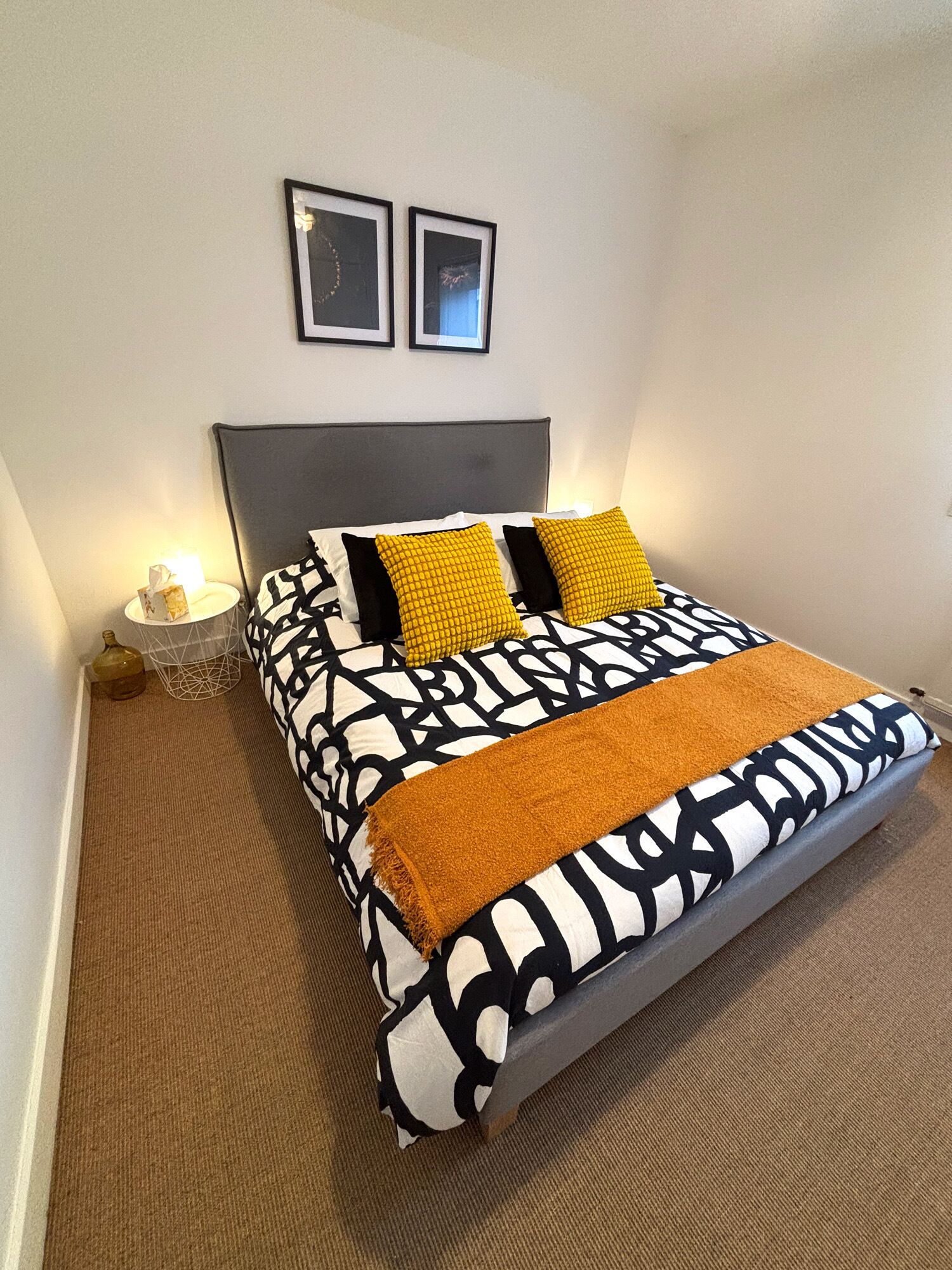 A bedroom with a bed, a nightstand, a lamp, and two framed pictures on the wall.