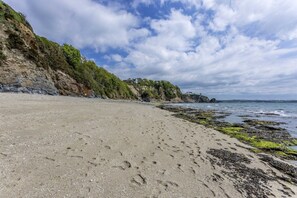 Una playa con costa rocosa, cielos despejados y huellas en la arena.