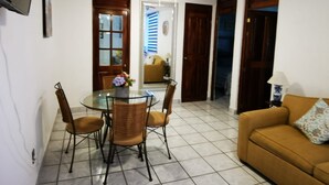 Un coin repas avec une table en verre et des chaises en osier, un ventilateur de plafond et un canapé agrémenté d’un coussin.