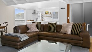 Una sala moderna con un sofá seccional de cuero marrón, una mesa de centro de vidrio y un comedor con mesa y sillas de madera.