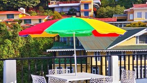 A terrace with a table and chairs, an umbrella, and a view of colorful buildings in the background. - Aurora The Mall Darjeeling (Darjeeling)