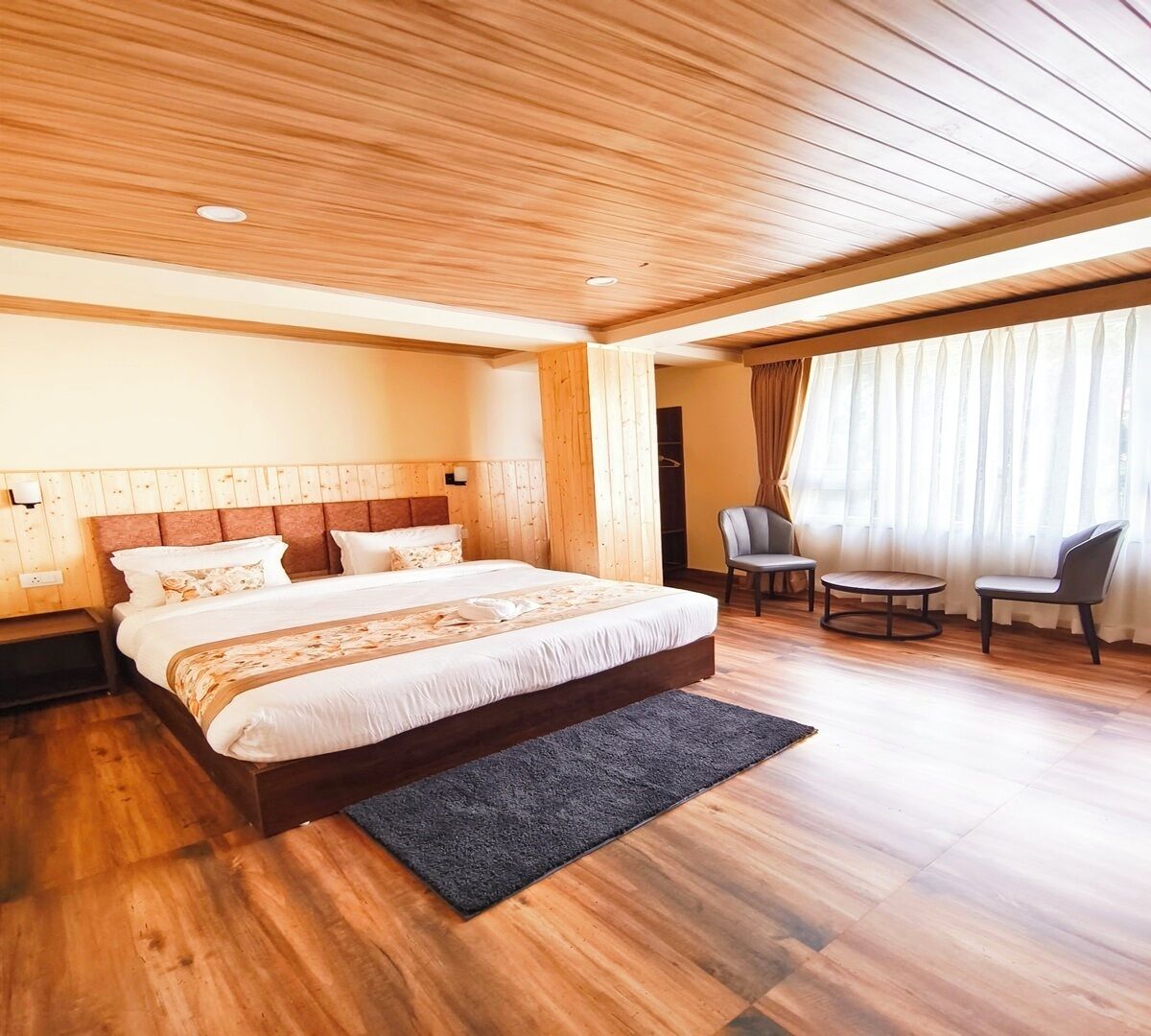 Un dormitorio amplio con una cama grande, techo de madera y un área de descanso con una mesa y sillas.