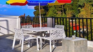 A terrace with a table and chairs under a multicolored umbrella, surrounded by a black railing and lush greenery in the background. - Aurora The Mall Darjeeling (Darjeeling)