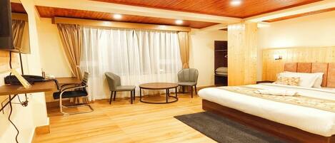 A hotel room with a wooden ceiling, a bed, a desk with a chair, and a small round table with two chairs.