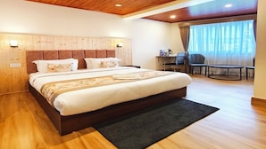 A modern bedroom with a wooden ceiling, a large bed, a desk, and a view of the outdoors. - Aurora The Mall Darjeeling (Darjeeling)