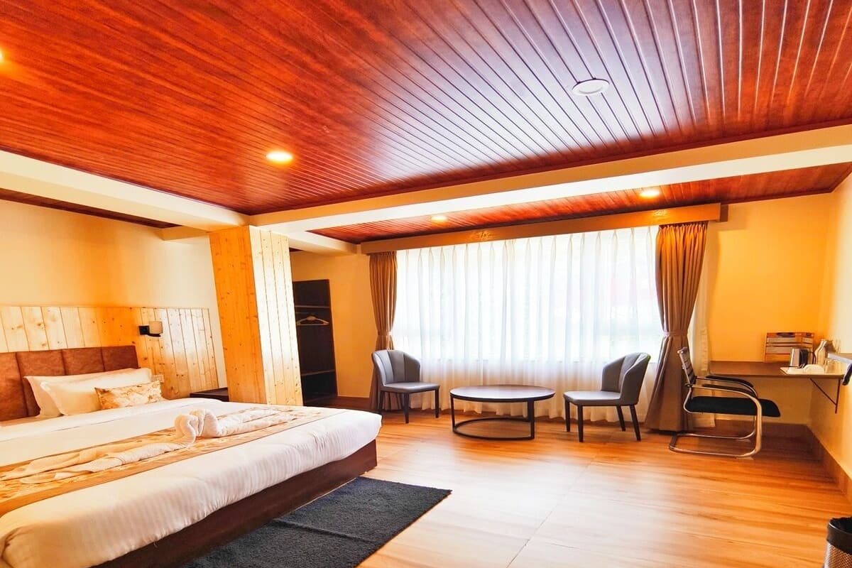 Quarto de hotel moderno com teto de madeira, uma cama grande, uma mesa de trabalho e um espaço de estar com cadeiras.