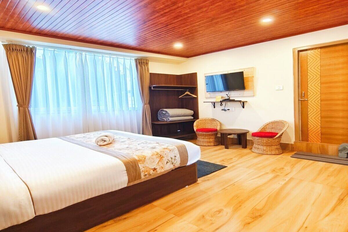 Quarto de hotel com teto de madeira, cama com colcha estampada e televisão fixada na parede, além de uma porta de madeira.