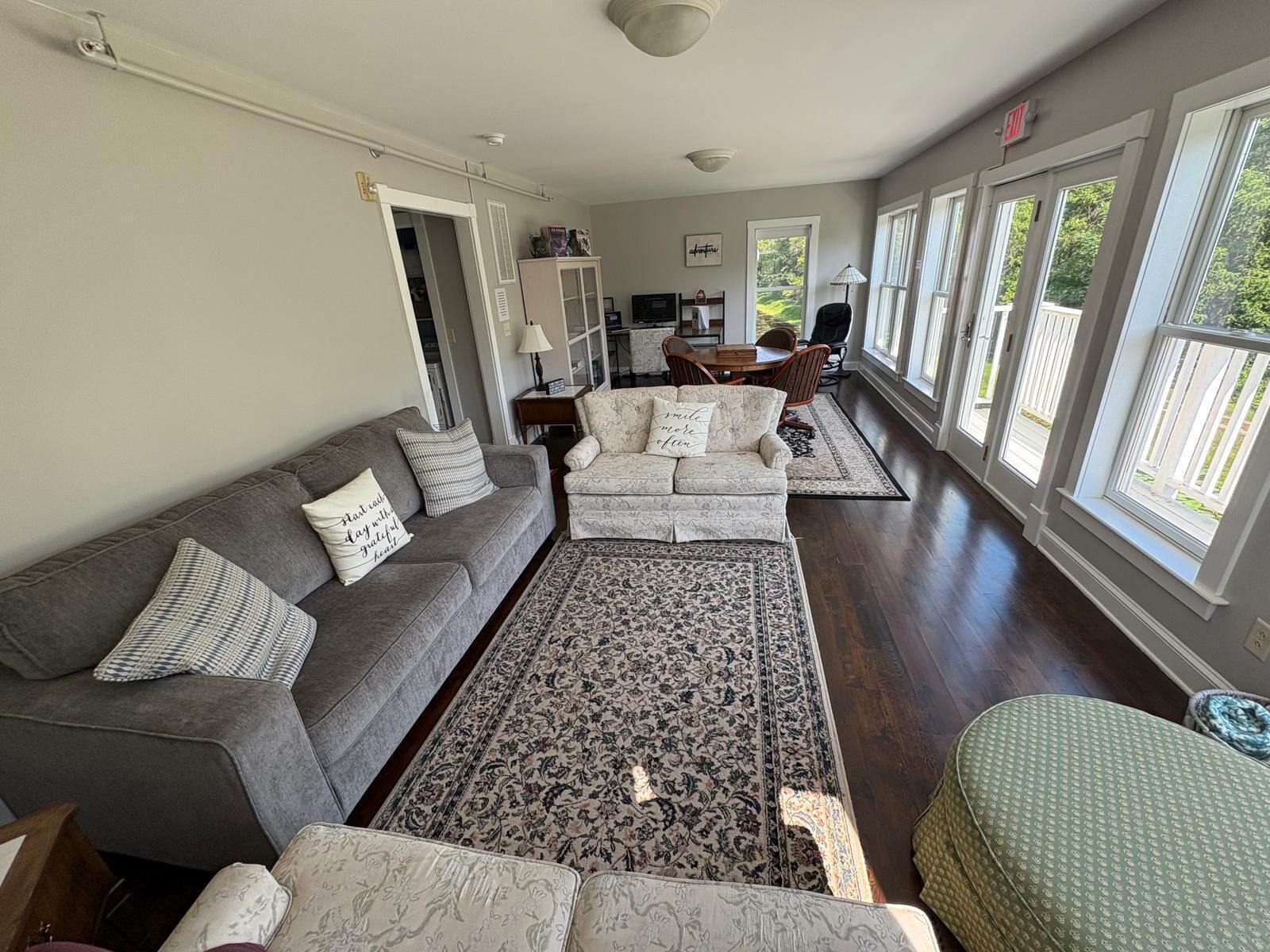 A spacious living room with a grey sofa, patterned armchairs, a large rug, and a dining area with a table and chairs.