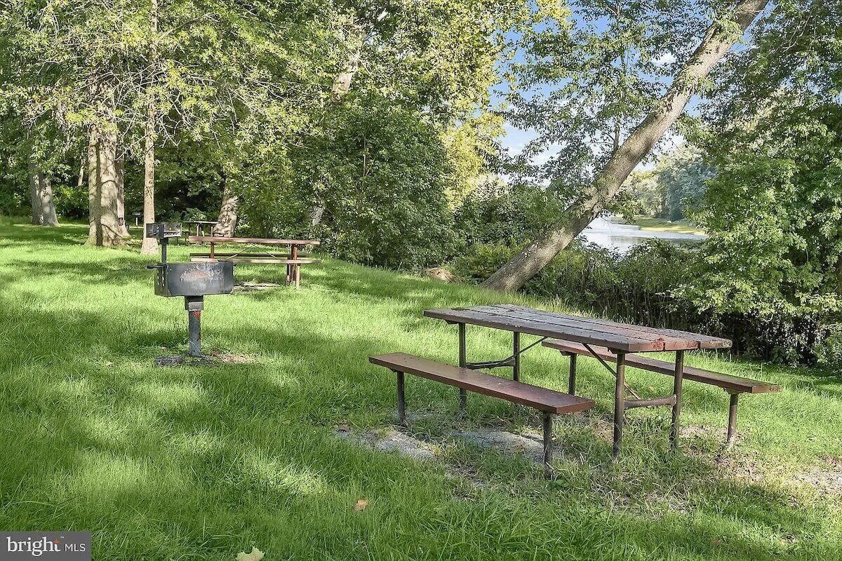 A picnic area with a wooden table and benches, surrounded by grass and trees.