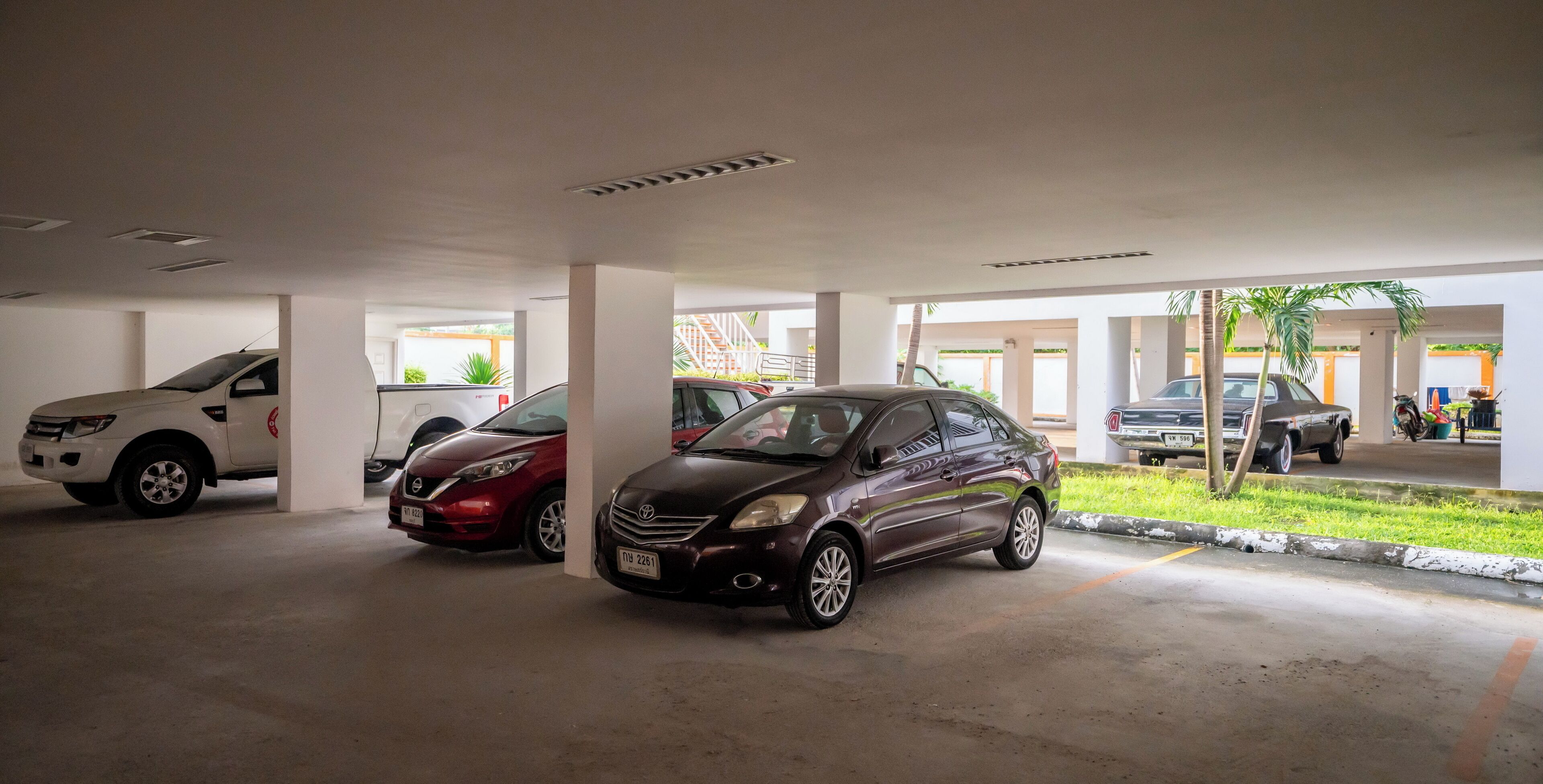 Un garaje para estacionar con varios coches bajo pilares blancos.