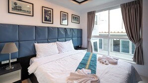Une chambre d’hôtel avec un grand lit, une tête de lit, une table de chevet, une lampe, une fenêtre avec des rideaux et des tableaux encadrés au mur.