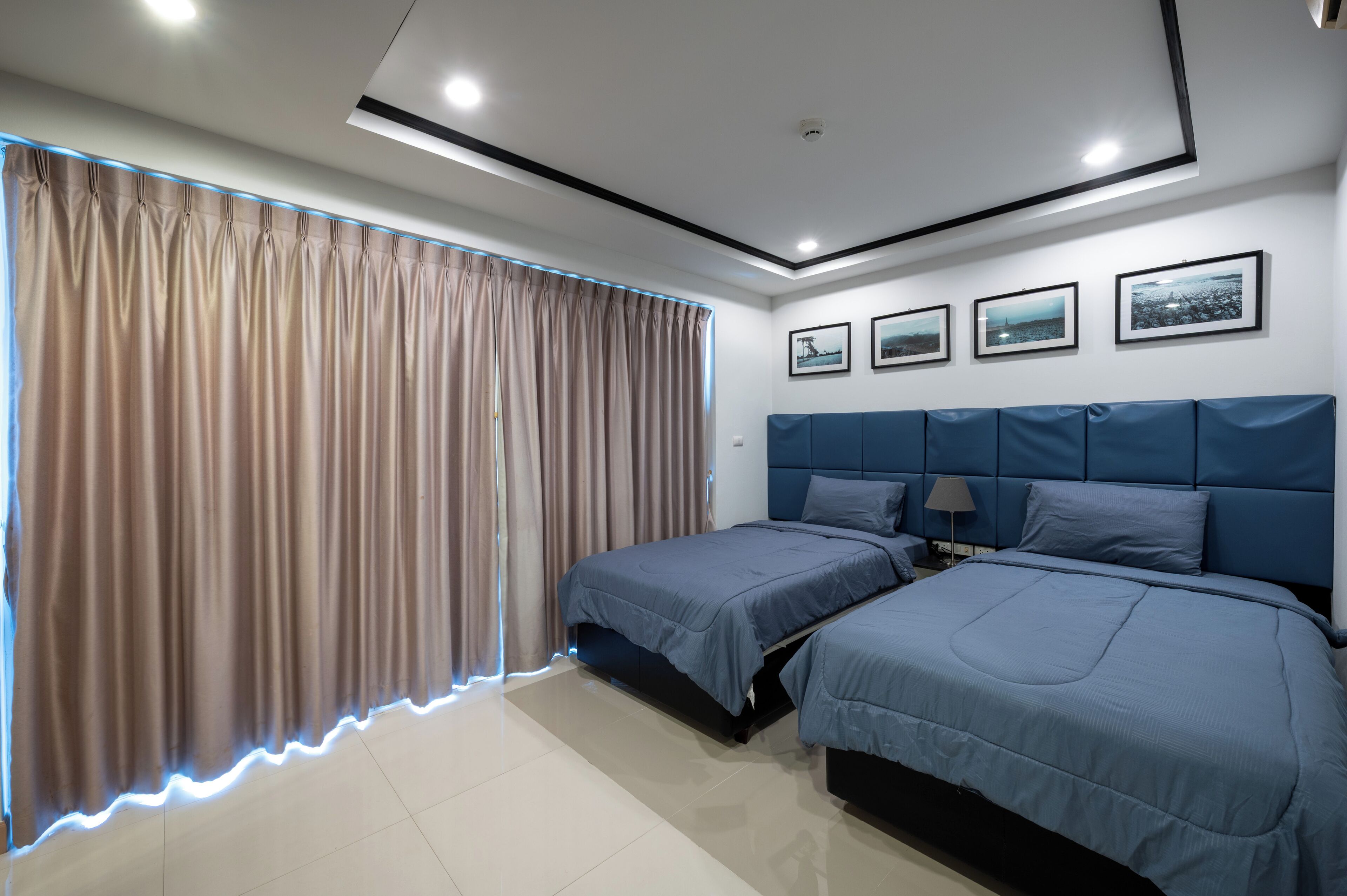 Une chambre moderne avec deux lits, une grande fenêtre avec des rideaux et trois tableaux encadrés accrochés au mur.