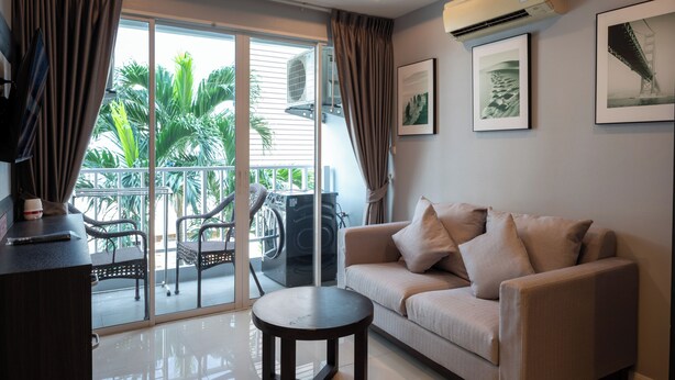 Un salon moderne comprenant un canapé, une table basse, un téléviseur et un balcon aménagé avec du mobilier d’extérieur.