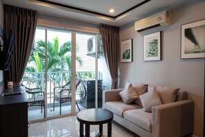 A modern living room with a sofa, a coffee table, a TV, and a balcony with outdoor furniture. - New Nordic Club 1 by Apartwell (Pattaya)