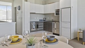 A modern kitchen with white cabinetry, stainless steel appliances, and a dining area with a table set for two. - Water Views Apartment | Stylish 3BR Villa with Pool & Lake Access (Taupō)