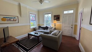 A cozy living room with a sofa, a coffee table, and a lamp. There are two windows with views of trees and a door with a window. - Charming 2-bedroom house, with large greatroom, quiet Avenues neighborhood (Salt Lake City)