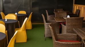A room with round tables and yellow chairs, wicker furniture, and a green carpet. - Noaz Hotel  (Kampala)