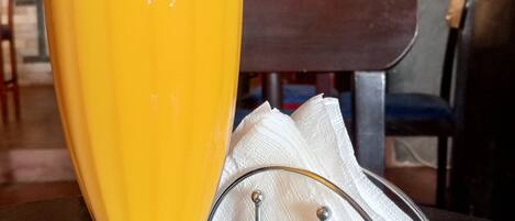 A tall glass of orange juice with a pink straw on a table, accompanied by a napkin and a metal napkin holder.