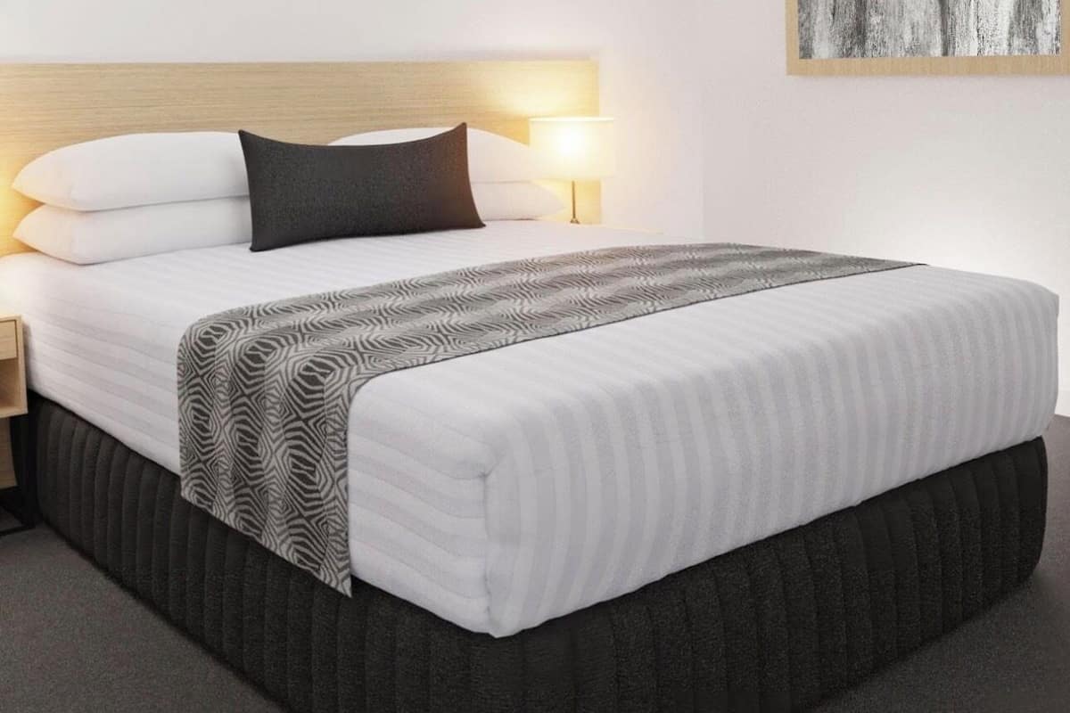 A hotel room with a bed, a nightstand, a lamp, and a wall-mounted artwork.