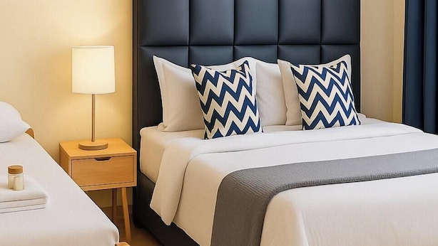 A hotel room with a bed, a nightstand, a lamp, and a bedside table. - Noaz Hotel  (Kampala)