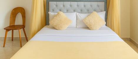 A bed with a tufted headboard, two pillows, and a wooden chair.