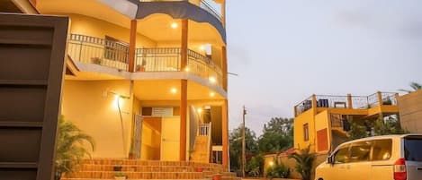 A multi-story building with balconies, a staircase, and a parked car.