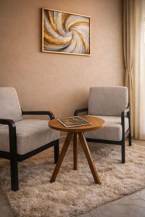 A room with two armchairs, a round wooden table, and a large abstract painting on the wall. - Noaz Hotel (Kampala)