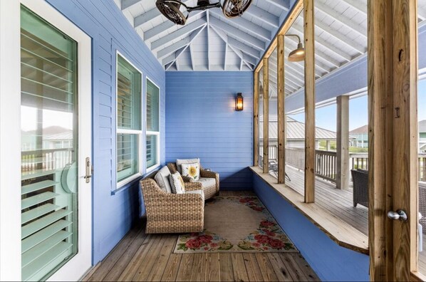A covered porch with blue walls, wicker furniture, and a wooden floor.