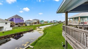 A residential area with houses along a canal, a wooden deck, and a clear sky. - Charming 2-bedroom cabin in serene Crystal Beach (Bolivar Peninsula)