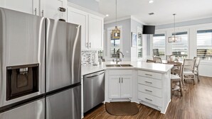 A modern kitchen with white cabinetry, stainless steel appliances, and a dining area with wooden chairs. - Charming 2-bedroom cabin in serene Crystal Beach (Bolivar Peninsula)