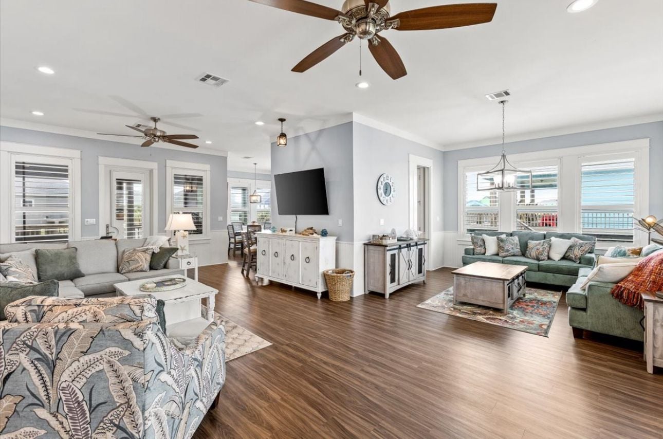A spacious living room with hardwood flooring, a ceiling fan, a flat-screen TV, and a dining area with a chandelier.