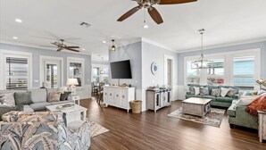 A spacious living room with hardwood flooring, a ceiling fan, a flat-screen TV, and a dining area with a chandelier. - Charming 2-bedroom cabin in serene Crystal Beach (Bolivar Peninsula)