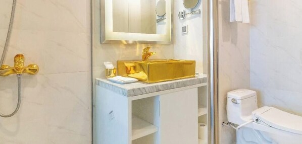 A bathroom with a gold sink, a toilet, and a shower. - Apartment hotel at wyndham golden bay có ban công máy giặt (Đà Nẵng)