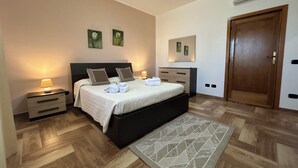 A bedroom with a bed, bedside tables, a dresser, a rug, and a door. - Villa Eugenie with pool (Sardegna)