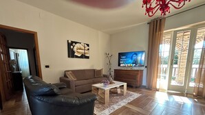 A living room with a black leather sofa, a wooden coffee table, and a television on a wooden cabinet. - Villa Eugenie with pool (Sardegna)