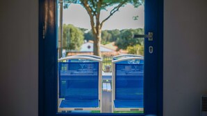 A view from inside a room with two blue beds, a window, and a door.