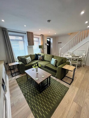 A modern living room with a green sofa, a coffee table with a vase, and a staircase leading to another level. - Monthly Stay 3 bed Bike Store Contractors (Treharris)