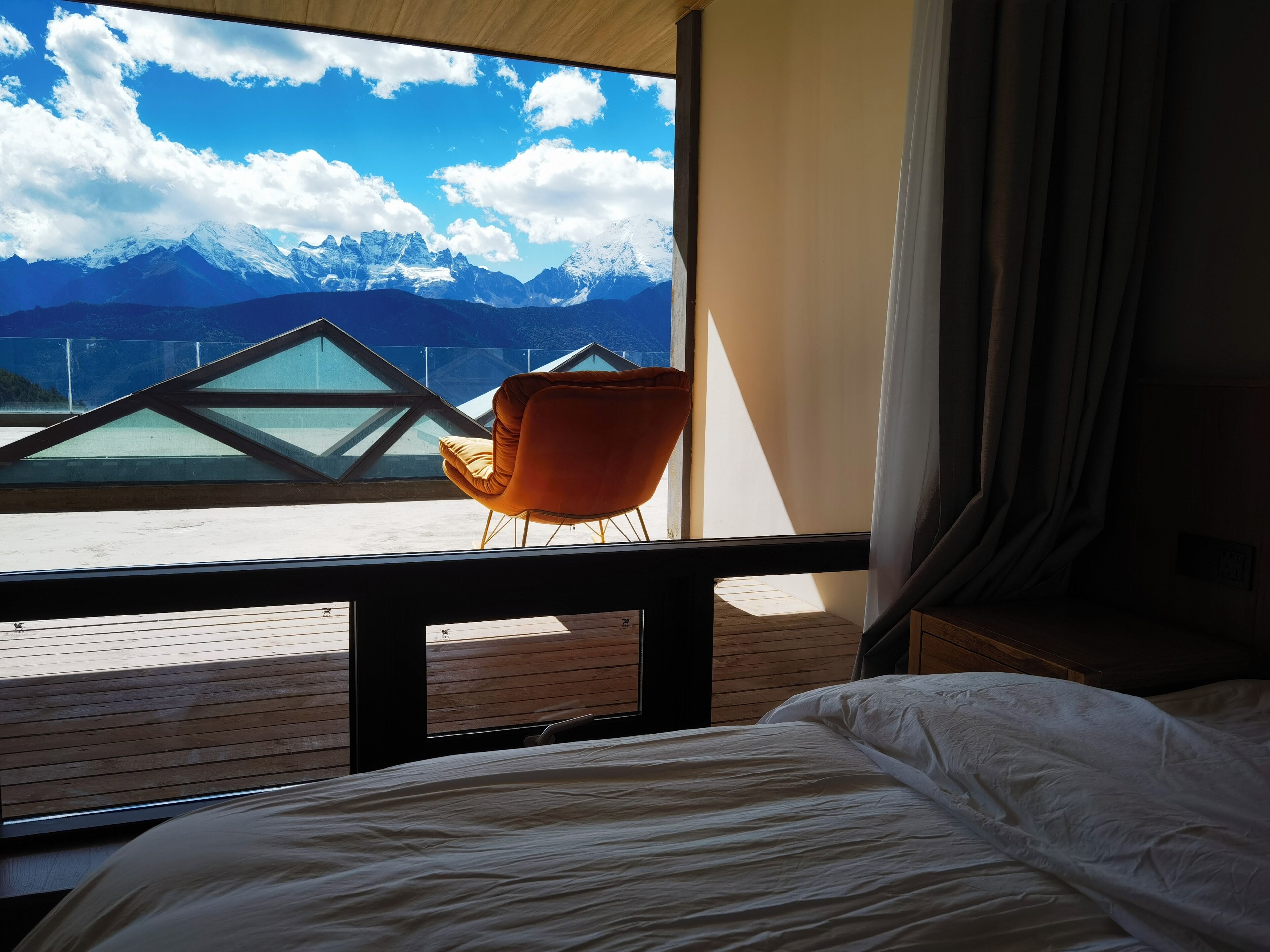 A room with a bed, a window with a view of snow-capped mountains, and a chair.